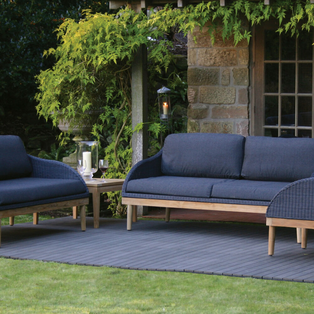 a lifestyle shot of the Harris outdoor seating range in a modern garden. The armchair and sofas are slate grey with teak legs and seat and back pads.